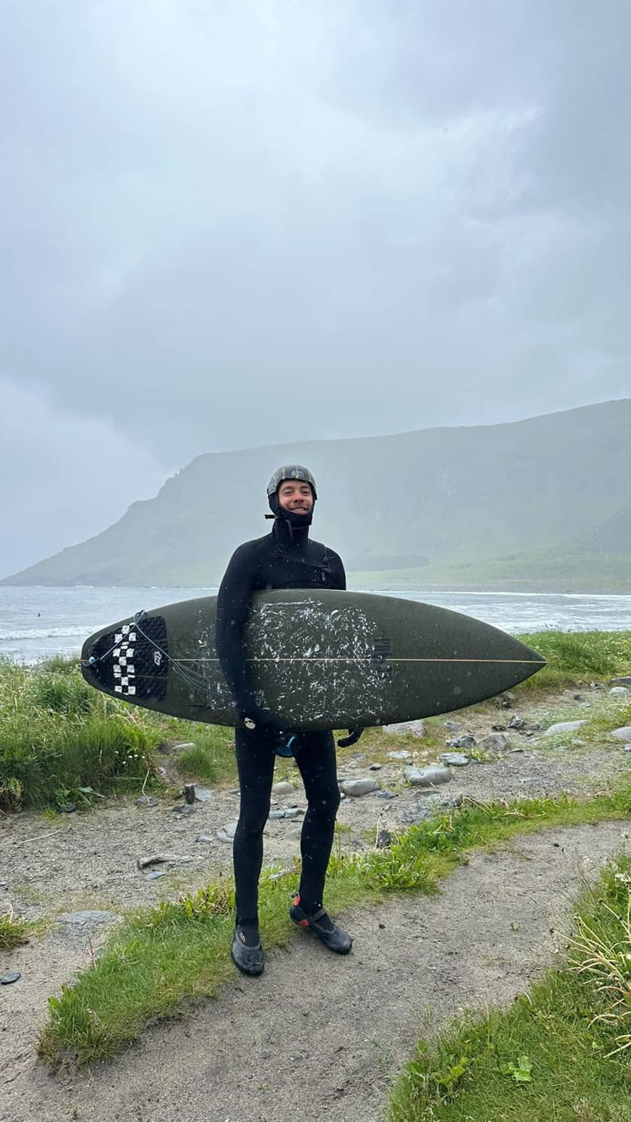 Customer wearing a prototype soft surf helmet while holding his surfboard at a surf break in the North of Norway.