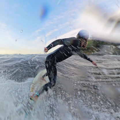 Surfer on a wave spraying water into the camera while wearing the soft and comfortable surf helmet by Sjø.Protection.