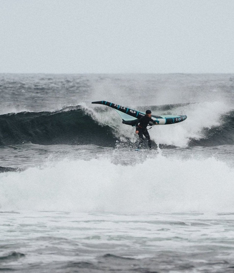 Wing foiler surfing a wave wearing the soft Kevlar reinforced surf helmet by Sjø Protection.